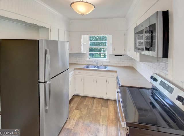 kitchen with stainless steel appliances, a sink, white cabinets, light countertops, and crown molding