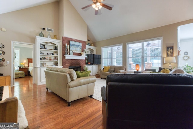 living room featuring high vaulted ceiling, ceiling fan, hardwood / wood-style flooring, and a brick fireplace