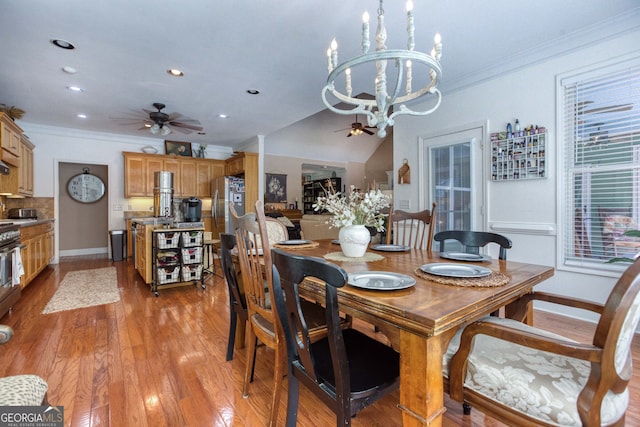 dining space with lofted ceiling, ceiling fan with notable chandelier, hardwood / wood-style flooring, and crown molding