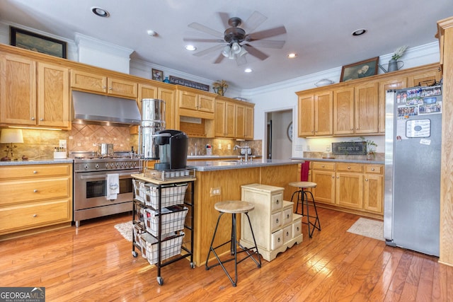 kitchen featuring a breakfast bar area, an island with sink, stainless steel appliances, ceiling fan, and light wood-type flooring