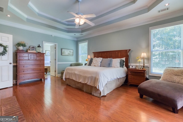 bedroom featuring crown molding, hardwood / wood-style flooring, ceiling fan, and a tray ceiling