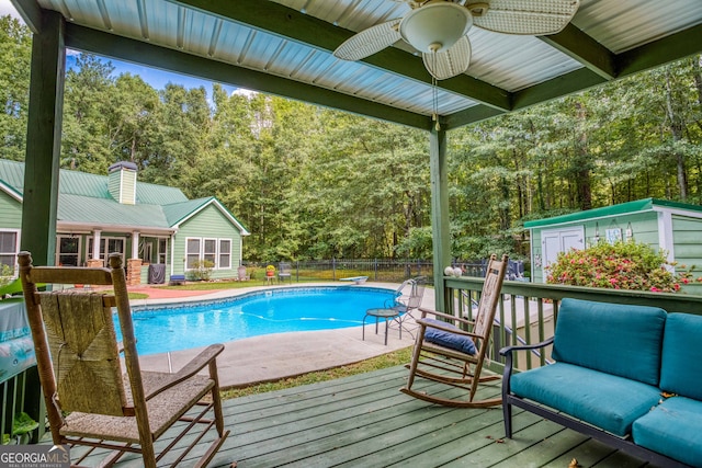 view of pool with an outdoor structure, a deck, a diving board, and ceiling fan