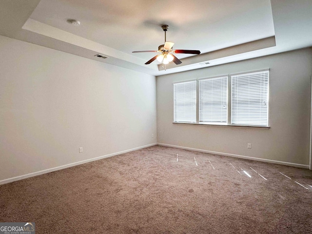 unfurnished room with a raised ceiling, ceiling fan, and carpet flooring