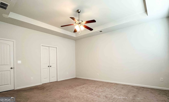 carpeted spare room with a raised ceiling and ceiling fan