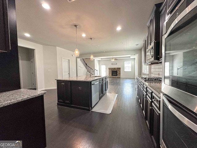 kitchen with appliances with stainless steel finishes, dark hardwood / wood-style floors, a fireplace, and an island with sink