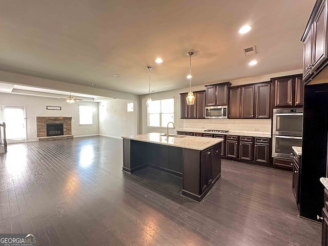 kitchen with dark hardwood / wood-style flooring, a fireplace, pendant lighting, appliances with stainless steel finishes, and an island with sink