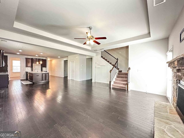 unfurnished living room featuring a fireplace, sink, ceiling fan, dark hardwood / wood-style floors, and a tray ceiling