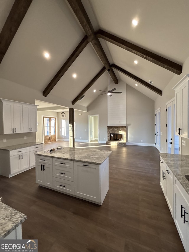 kitchen featuring white cabinets, a kitchen island, a fireplace, beam ceiling, and dark hardwood / wood-style flooring