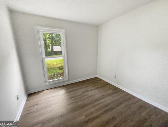 spare room with baseboards and dark wood-type flooring