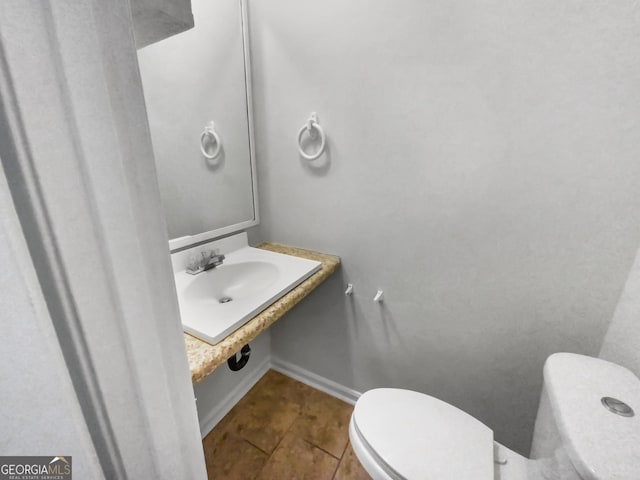 half bathroom featuring a sink, tile patterned flooring, toilet, and baseboards