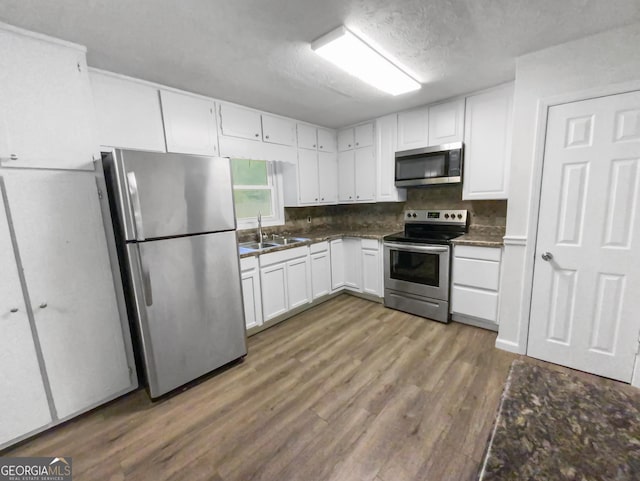 kitchen with appliances with stainless steel finishes, white cabinetry, a sink, and wood finished floors