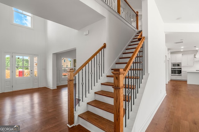 staircase with visible vents, baseboards, a towering ceiling, wood finished floors, and recessed lighting