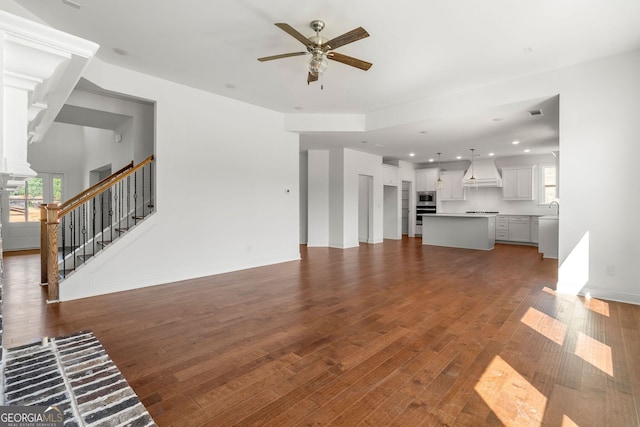 unfurnished living room with dark wood-style flooring, ceiling fan, baseboards, and stairs