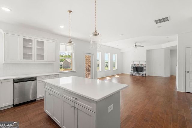 kitchen featuring a kitchen island, white cabinets, light countertops, stainless steel dishwasher, and glass insert cabinets