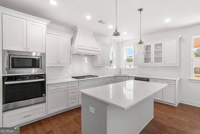 kitchen featuring custom range hood, glass insert cabinets, a center island, stainless steel appliances, and light countertops