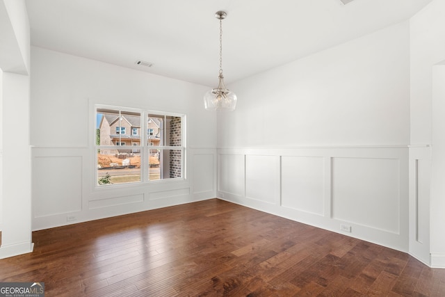 unfurnished dining area featuring a notable chandelier, visible vents, a decorative wall, and dark wood-type flooring