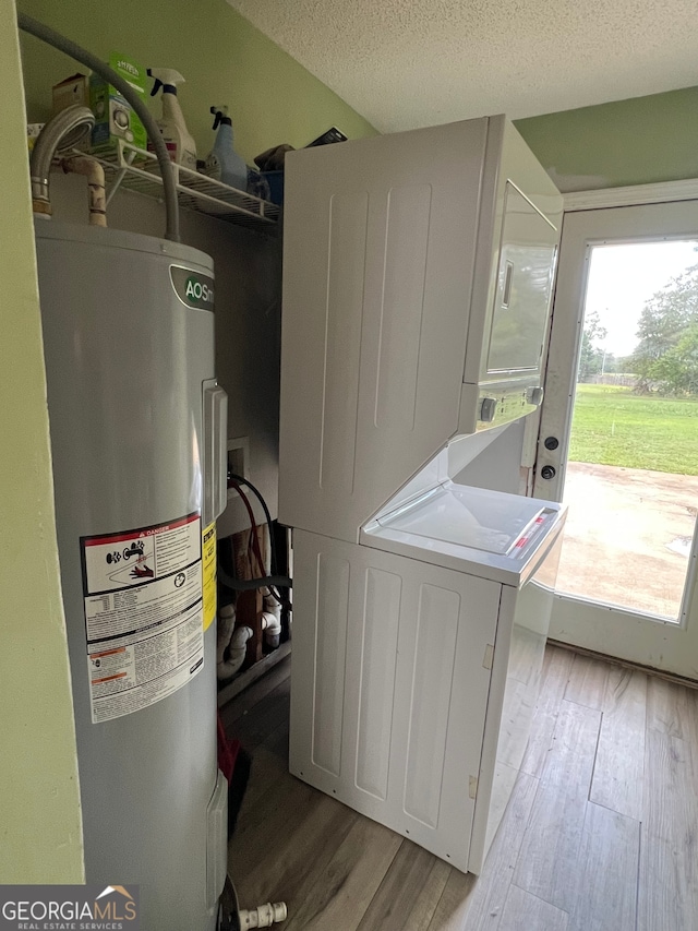 laundry area featuring a textured ceiling, water heater, stacked washing maching and dryer, and light hardwood / wood-style flooring