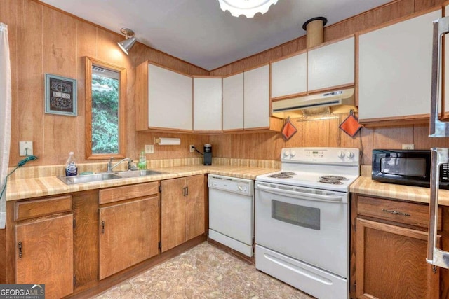 kitchen with a sink, light countertops, white appliances, under cabinet range hood, and wood walls