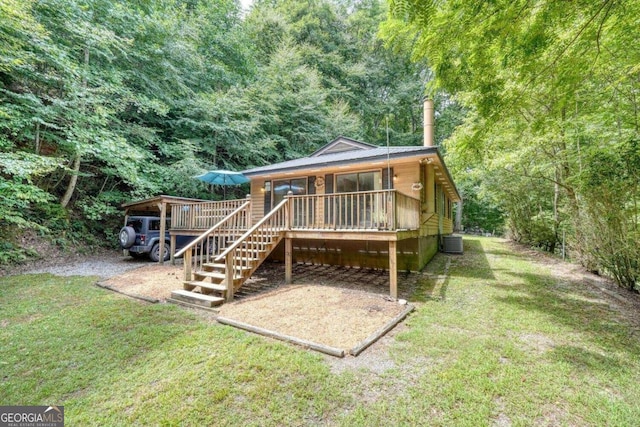 back of property with metal roof, central AC, a forest view, and a lawn