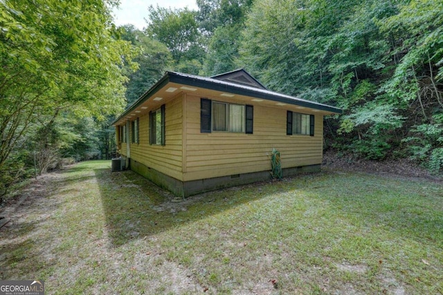 view of side of home with a forest view, crawl space, central AC, and a lawn