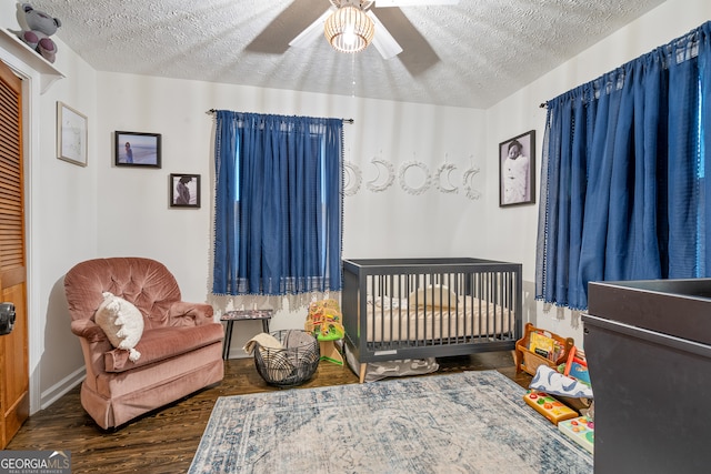 bedroom featuring a textured ceiling, ceiling fan, dark hardwood / wood-style flooring, and a crib