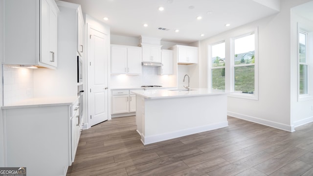 kitchen with a center island with sink, decorative backsplash, white cabinetry, and hardwood / wood-style floors