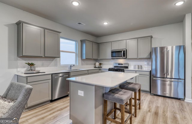 kitchen with light wood finished floors, a sink, gray cabinetry, stainless steel appliances, and a kitchen bar