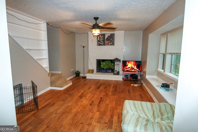 living room featuring hardwood / wood-style floors, brick wall, a textured ceiling, ceiling fan, and a brick fireplace