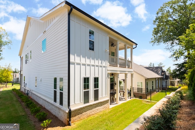 rear view of house with ceiling fan, a balcony, and a lawn