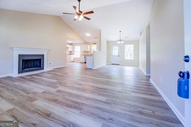 unfurnished living room with ceiling fan with notable chandelier, high vaulted ceiling, and light hardwood / wood-style floors