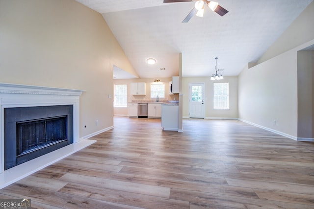 unfurnished living room with ceiling fan with notable chandelier, high vaulted ceiling, sink, and light hardwood / wood-style flooring