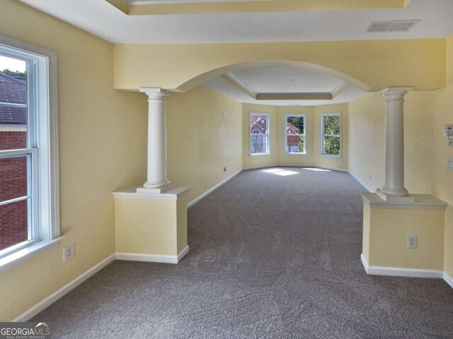 unfurnished room with a raised ceiling, carpet floors, a healthy amount of sunlight, and decorative columns