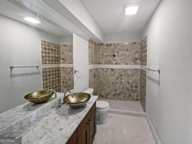 bathroom featuring tile patterned flooring, toilet, a tile shower, and vanity