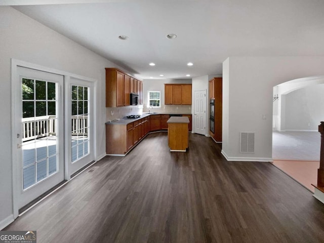 kitchen with appliances with stainless steel finishes, backsplash, dark wood-type flooring, and a kitchen island