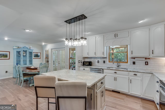 kitchen featuring white cabinetry, light stone counters, sink, hanging light fixtures, and light hardwood / wood-style floors