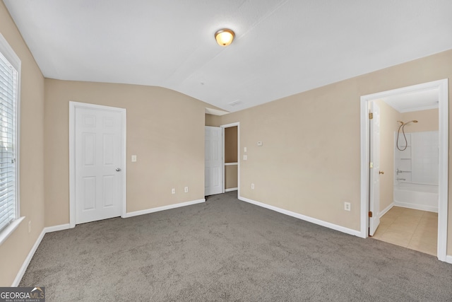 unfurnished bedroom with multiple windows, carpet, connected bathroom, and vaulted ceiling