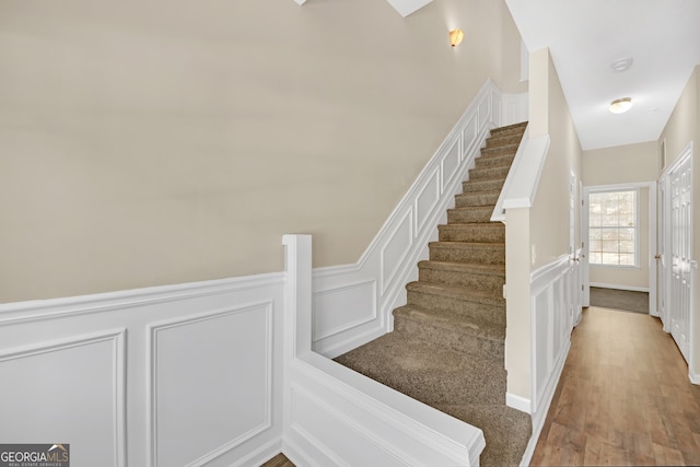 stairway with a decorative wall, wainscoting, and wood finished floors