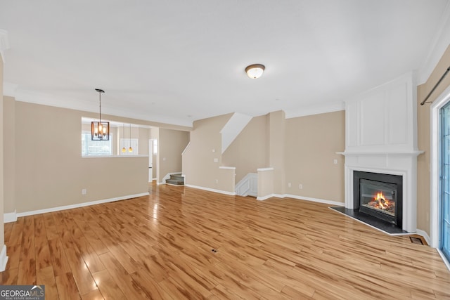 unfurnished living room with light wood-type flooring, a large fireplace, a notable chandelier, and ornamental molding