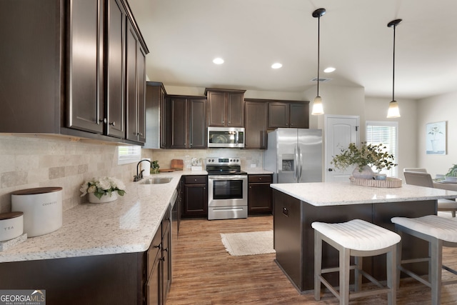 kitchen with light hardwood / wood-style floors, a kitchen island, sink, hanging light fixtures, and appliances with stainless steel finishes