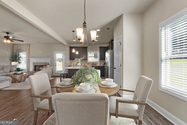 dining space featuring ceiling fan with notable chandelier, a fireplace, dark hardwood / wood-style floors, and a healthy amount of sunlight