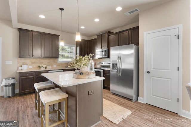 kitchen featuring pendant lighting, appliances with stainless steel finishes, a center island, light wood-type flooring, and a kitchen bar