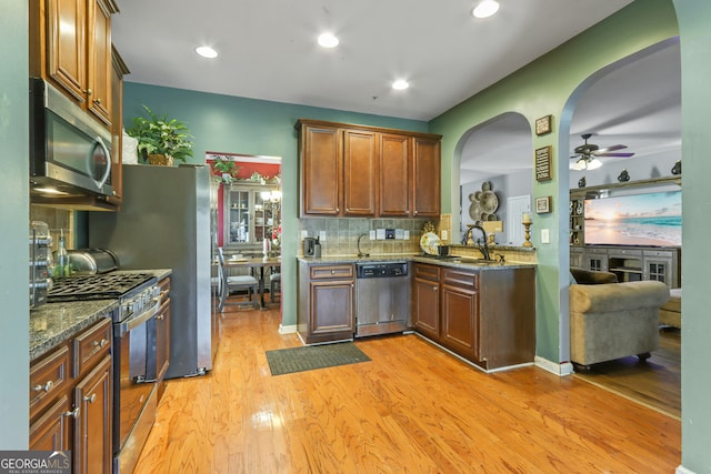 kitchen featuring light hardwood / wood-style flooring, appliances with stainless steel finishes, sink, ceiling fan, and dark stone counters