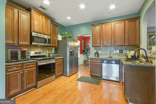 kitchen with dark stone countertops, light hardwood / wood-style flooring, backsplash, stainless steel appliances, and sink