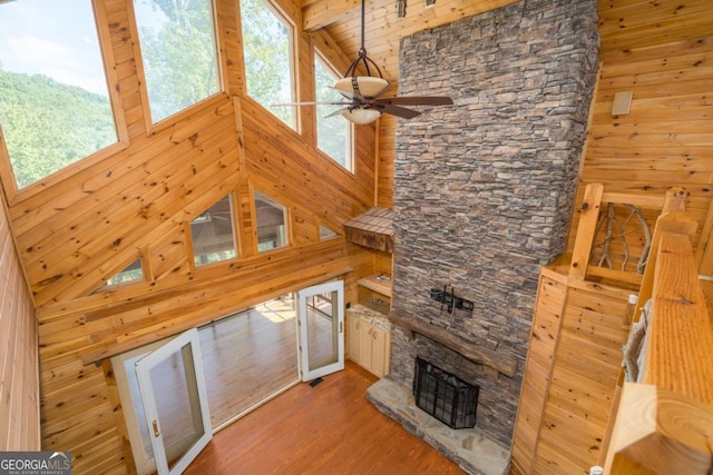 unfurnished living room featuring a stone fireplace, a wealth of natural light, high vaulted ceiling, and hardwood / wood-style flooring