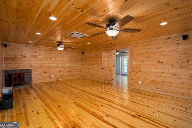 unfurnished living room featuring wooden ceiling, a stone fireplace, wooden walls, ceiling fan, and light wood-type flooring