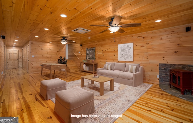 living room with a wood stove, wooden ceiling, light hardwood / wood-style flooring, and wooden walls