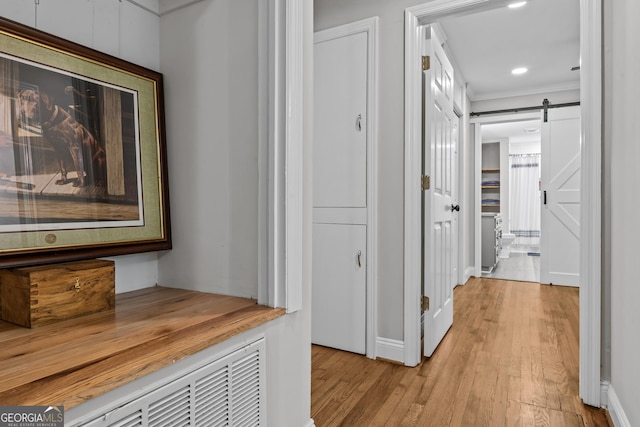 hall featuring ornamental molding, light wood finished floors, and a barn door