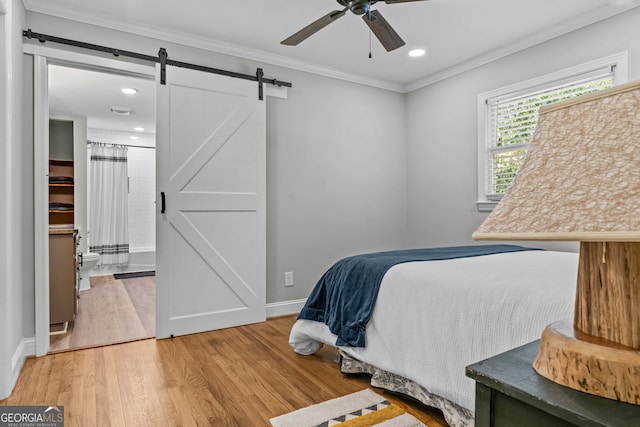 bedroom featuring a barn door, ornamental molding, a ceiling fan, wood finished floors, and baseboards