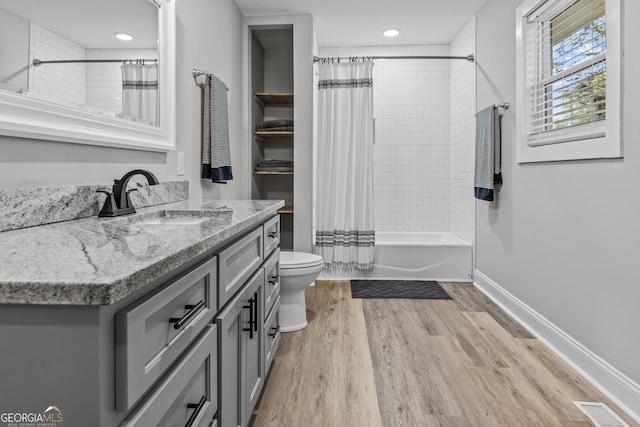 full bath featuring visible vents, shower / bath combo, vanity, wood finished floors, and baseboards