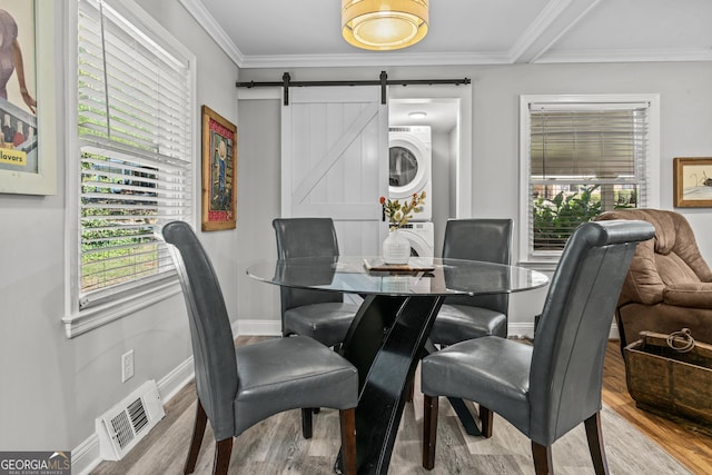 dining room featuring a barn door, wood finished floors, visible vents, stacked washer / drying machine, and crown molding